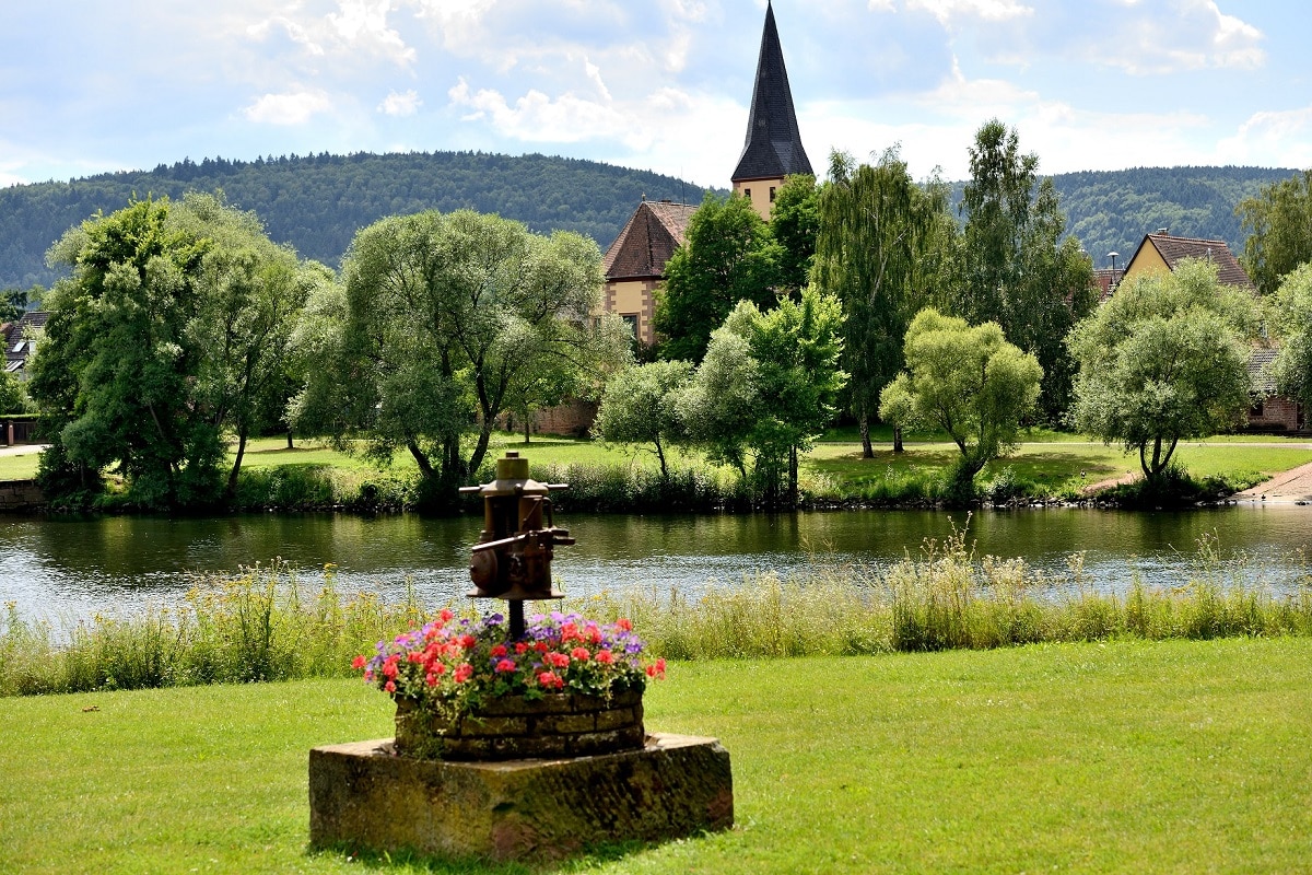 Blick von Großheubach auf das Kleinheubacher Mainufer, im Vordergrund eine mit Blumen bepflanzte Weinpresse