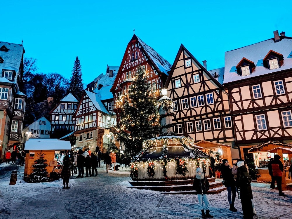 Marktplatz mit Schnee bedeckt. Im Rahmen vom Weihnachtsmarkt stehen einzelne Buden und ein schön dekorierter Weihnachtsbaum.