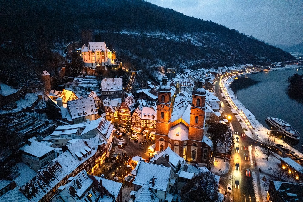 Drohnenaufnahme über dem Marktplatz. Miltenberg ist mit Schnee bedeckt und der Weihnachtsmarkt leuchtet im Dunkeln.