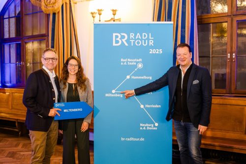 Bernd Kahlert, Janina Weber und Markus Riese vor einer Tafel mit der Streckenführung der BR Radltour 2025