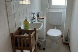 Schmales Badezimmer mit Toilette und Waschbecken.
