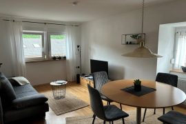 Esstisch im Vordergrund mit einem Sofa links und dem Fernseher rechts.