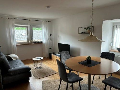 Esstisch im Vordergrund mit einem Sofa links und dem Fernseher rechts.