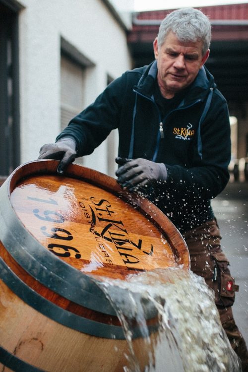 Mitarbeiter der St. Kilian Destille in Rüdenau hantiert bei Regen mit einem Whiskyfass